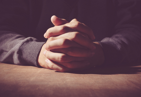 Praying hands of young man on a wooden desk background.の写真素材