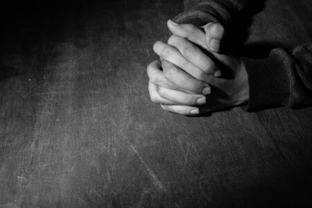 Praying hands of young man on a wooden desk background.の写真素材