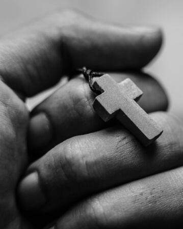 Closeup of praying hand holding the wooden cross.