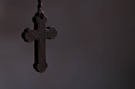 Rustic wooden cross hanging against soft dark background.