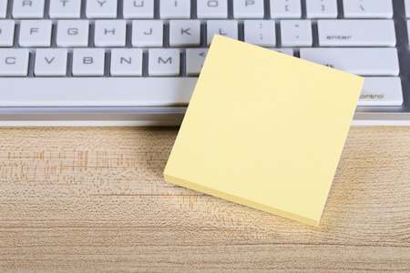 Blank yellow sticky note with keyboard on the wooden desk.の写真素材