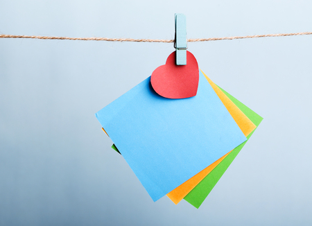 Blank sticky notes with red heart hanging against light blue background.