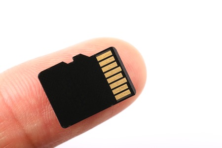 Micro SD memory card with finger against white background.