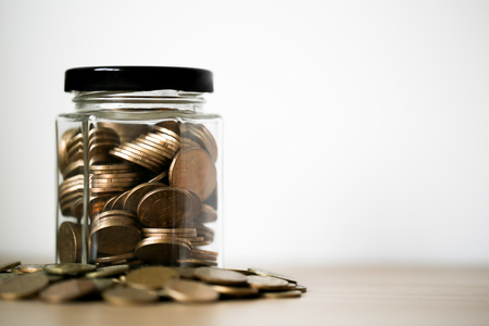 A lot coins in glass money jar against white background.