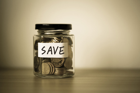 A lot coins in glass money jar with blank white paper on table.の写真素材