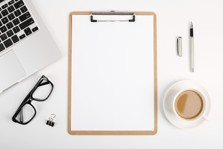 Workspace with blank clip board, laptop keyboard, office supplies, pen, glasses and coffee cup on white background. Flat lay, top view office table desk.の写真素材
