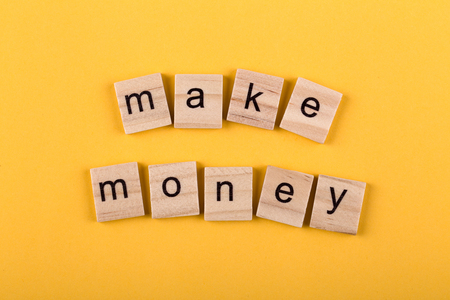Make money concept wooden blocks isolated on yellow background.の写真素材