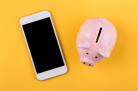 Piggy Bank With Smartphone on the yellow background.の写真素材