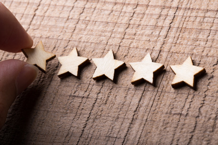 Hand putting wooden five star shape on table. The best excellent business services rating customer...