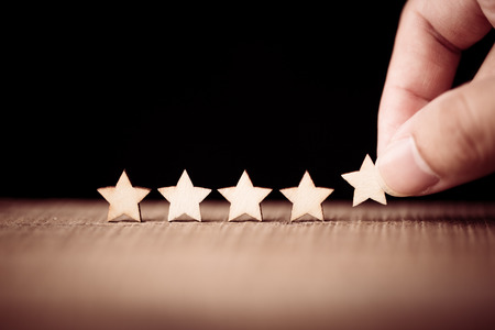Hand putting wooden five star shape on table. The best excellent business services rating customer...