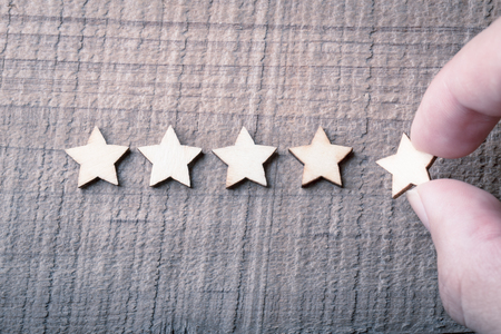 Hand putting wooden five star shape on table. The best excellent business services rating customer...