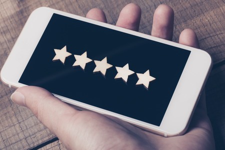 Hand holding smartphone with wooden five star shape. The best excellent business services rating...