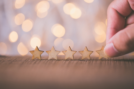 Hand putting wooden five star shape on table. The best excellent business services rating customer...