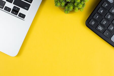 Topview of yellow office desktop with black glasses, laptop keyboard, calculator, green plant.の写真素材