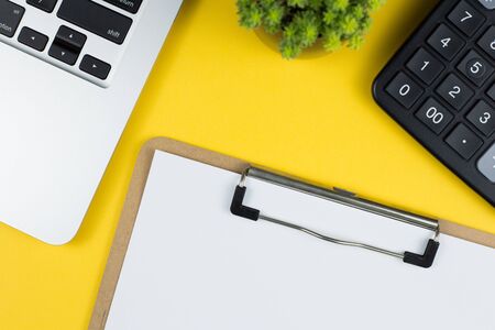 Topview of yellow office desktop with laptop keyboard, calculator, green plant and notepad.の写真素材
