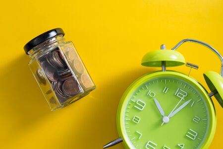 Alarm clock and a bottle of coins on yellow color background.の写真素材