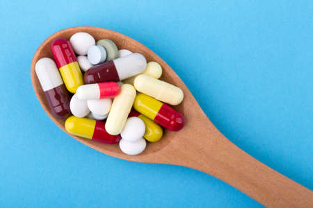 Assorted pharmaceutical medicine pills, tablets and capsules on wooden spoon with blue background.の写真素材