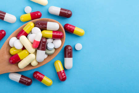 Assorted pharmaceutical medicine pills, tablets and capsules on wooden spoon with blue background.の写真素材