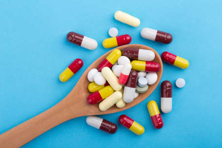 Assorted pharmaceutical medicine pills, tablets and capsules on wooden spoon with blue background.の写真素材