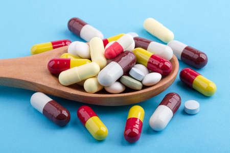 Assorted pharmaceutical medicine pills, tablets and capsules on wooden spoon with blue background.の写真素材