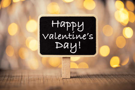 Valentine s Day greeting card. 14th of February. Happy Valentines Day Lettering written on blackboard with golden shine background. abstract background.の写真素材