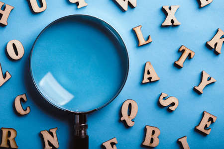Magnifying with wooden alphabets around on the blue background.の写真素材