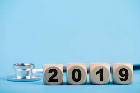 Stethoscope with 2019 wooden blocks on blue background.