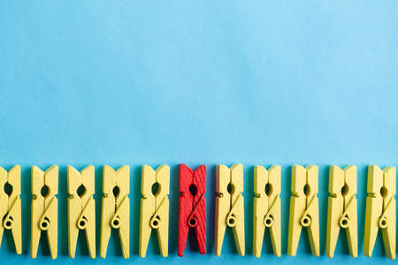 Stand out from the crowd and different concept. Leadership and other similar concepts. One red clothespin stands out from other yellow clothespins on blue background.の写真素材