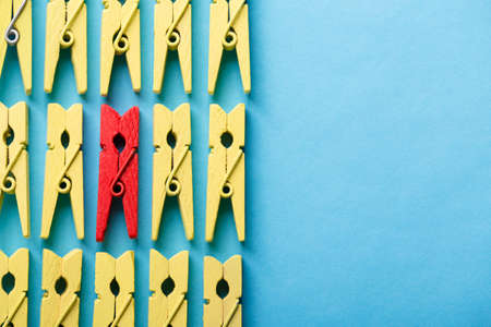 Stand out from the crowd and different concept. Leadership and other similar concepts. One red clothespin stands out from other yellow clothespins on blue background.の写真素材