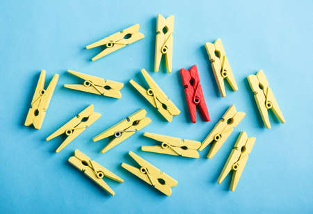 Stand out from the crowd and different concept. Leadership and other similar concepts. One red clothespin stands out from other yellow clothespins on blue background.の写真素材