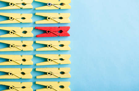 Stand out from the crowd and different concept. Leadership and other similar concepts. One red clothespin stands out from other yellow clothespins on blue background.の写真素材