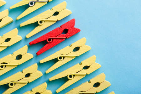 Stand out from the crowd and different concept. Leadership and other similar concepts. One red clothespin stands out from other yellow clothespins on blue background.の写真素材