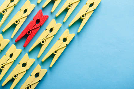 Stand out from the crowd and different concept. Leadership and other similar concepts. One red clothespin stands out from other yellow clothespins on blue background.の写真素材