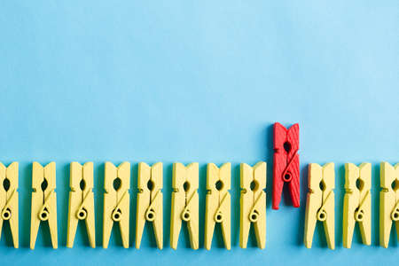Stand out from the crowd and different concept. Leadership and other similar concepts. One red clothespin stands out from other yellow clothespins on blue background.の写真素材