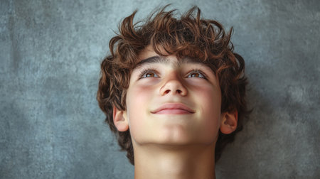 Portrait of a boy with curly hair looking up over gray backgroundの素材