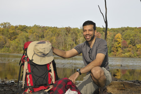 Young man with backpacking equipment outdoors with fall trees in background