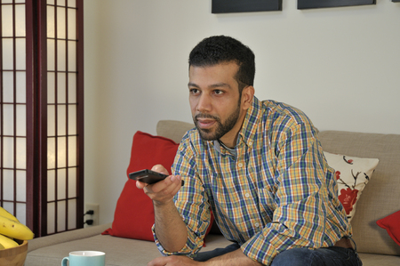 Young Hispanic many switching channels on TV with remote control at homeの写真素材