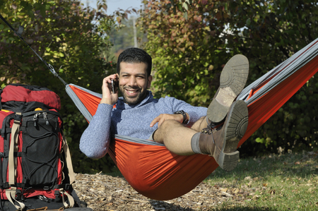 Happy Hispanic traveler having a conversation on mobile phone while laying in a hammock on vacationの写真素材