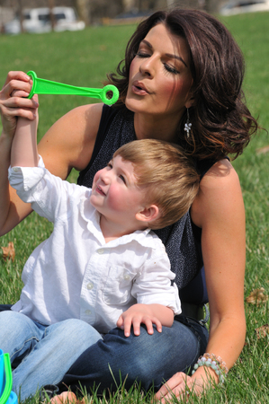 young mother blowing bubbles with her toddler son outsideの写真素材