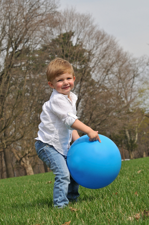 cute little blond boy playing outside with a big blue ballの写真素材