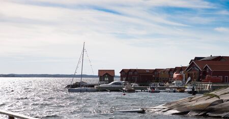 Small harbor on the swedish island of Karingon. Several boats are tied up at the pier and vacation homes in the background.の写真素材