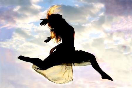 A young, attractive woman leaps through the air, with a beautiful cloudy sunset in the background.の写真素材