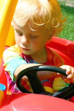a cute little boy driving a toy car on a sunny summer dayの写真素材
