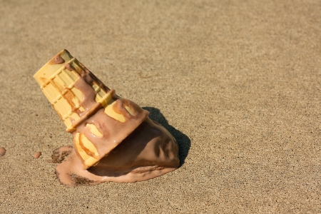 A melty chocolate ice cream cone has dropped upsidedown onto the sidewalk on a sunny sumer dayの写真素材