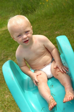 A cute baby boy sitting on a toy slide ready to slide into a kiddie pool on a hot summer dayの写真素材