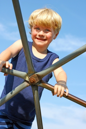 a cute little boy is smiling as he climbs a metal jungle gym at the playgroung on a sunny summer dayの写真素材