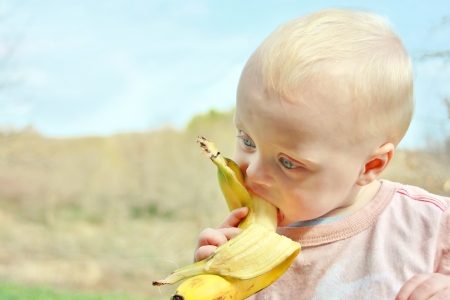 a cute baby boy is sitting outside in the country, eating a healthy banana fruitの写真素材