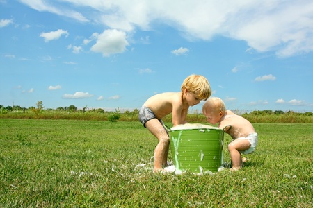 a young child and his baby brother are playing outside in a bucket full of bubbles and water on a sunny summer dayの写真素材