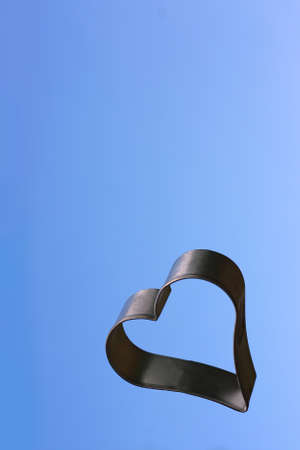 a silver heart shaped object is floating in the sky, isolated in front of a blue sky background, with copy space for textの写真素材