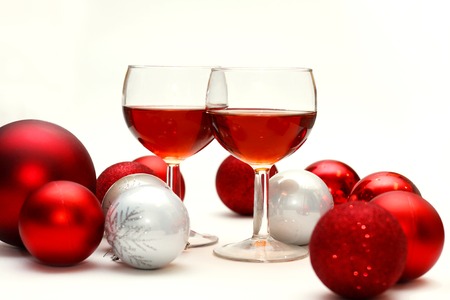 Two wine glasses filled with red wine sit on an isolated white background in surrounded by silver and red sparkling Christmas Bulb Decorationsの写真素材